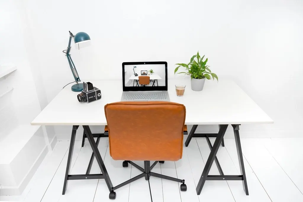 A laptop on a tidy home-office desk beside a window.